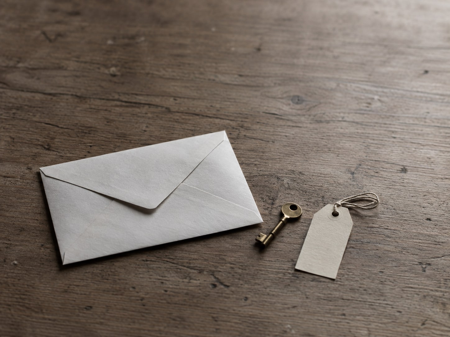 A sealed envelope, a small brass key and a blank paper tag lying on a plain wooden table.