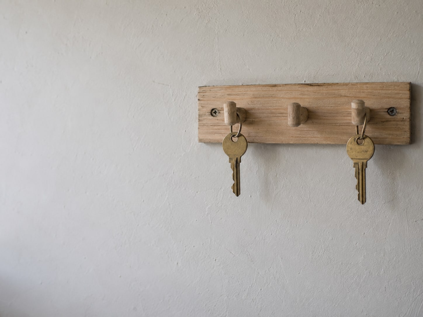 A row of identical plain office keys hanging from a wooden hook board, one hook left empty.