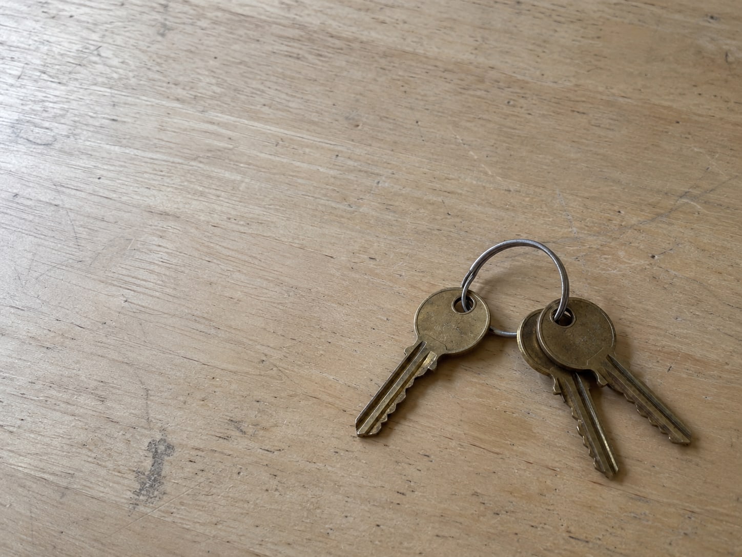 Three identical brass keys on a single ring resting on a plain desk, one key slightly apart from the others.