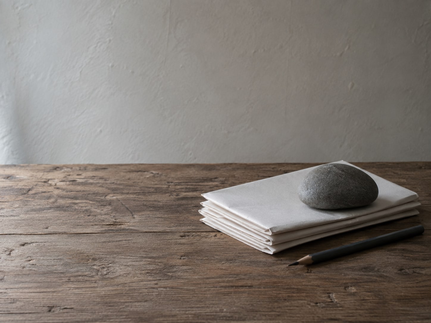 A small stack of folded blank invoices under a plain paperweight next to a pencil on a wooden table.