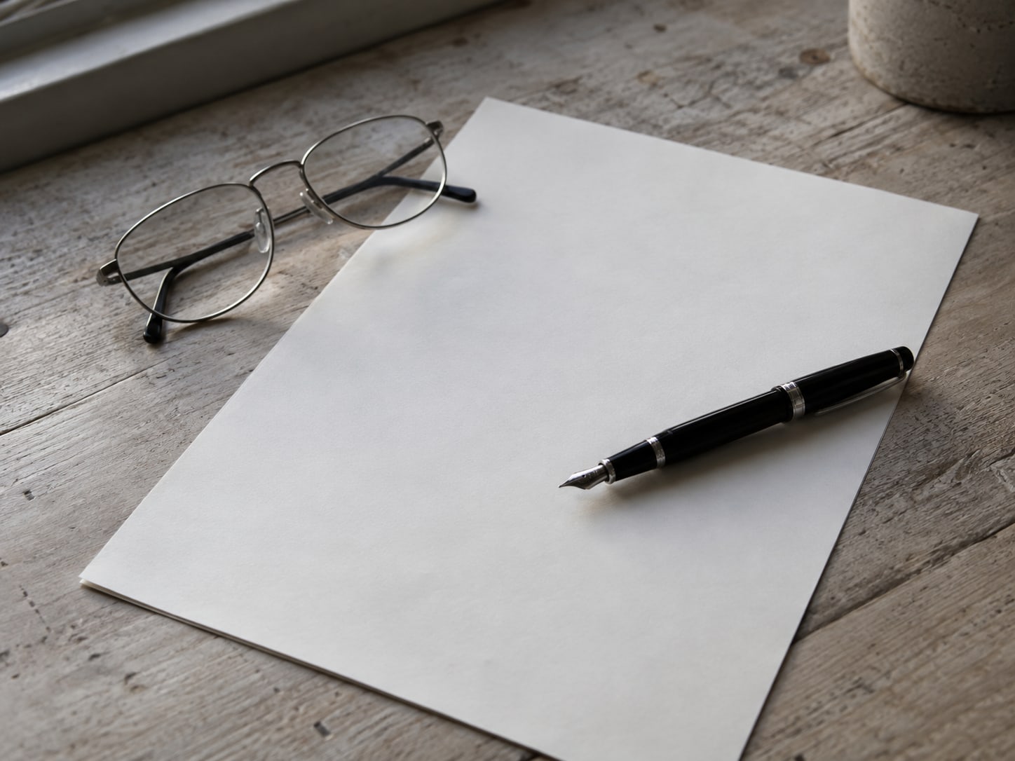 A fountain pen resting on an unsigned blank contract page beside a pair of reading glasses.