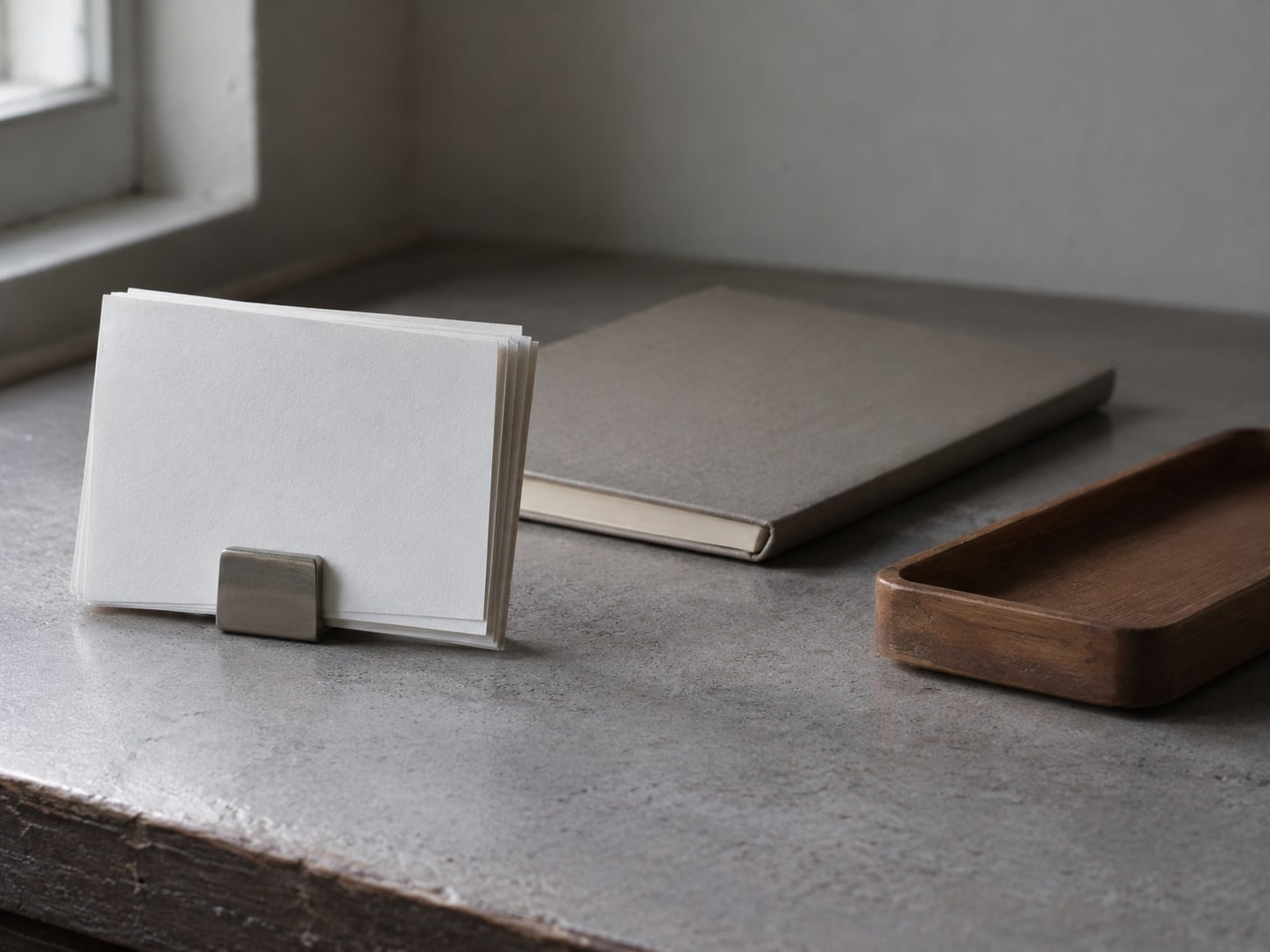 A small stack of blank index cards held by a clip next to a closed notebook and a wooden pen tray on a quiet counter.