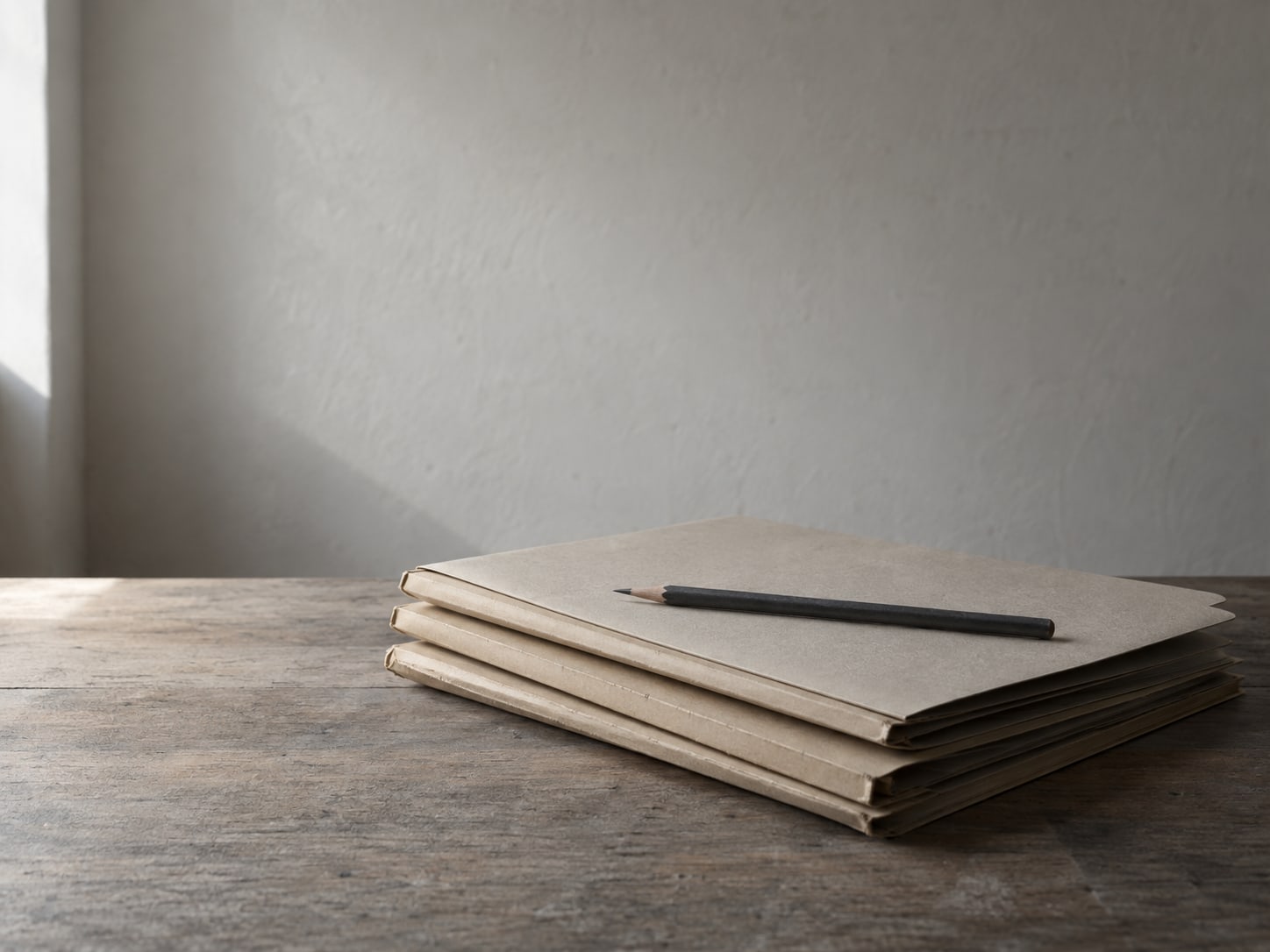 A tidy stack of three paper folders on a desk with a single pencil laid across the top.