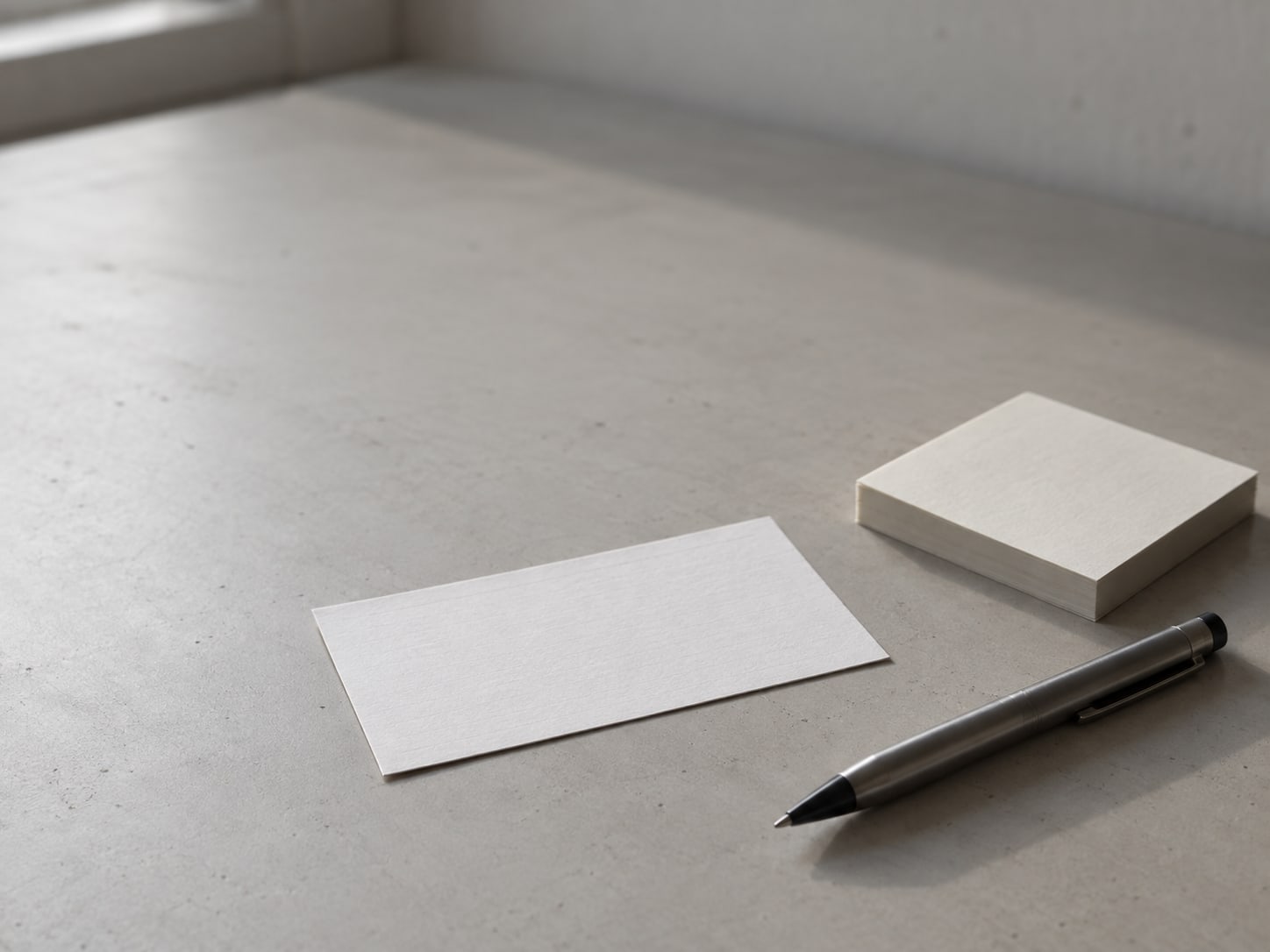 A single index card and a pen resting on a clean desk beside a stack of blank sticky notes.