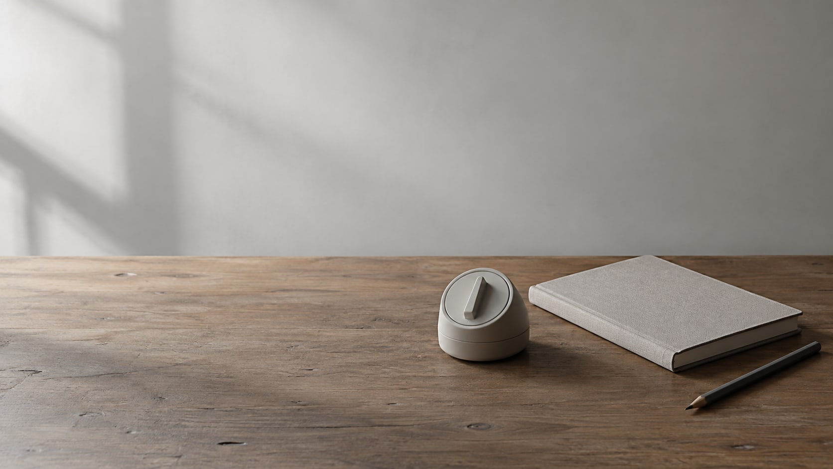 A small kitchen timer, a closed notebook and a pencil on a clean wooden desk.