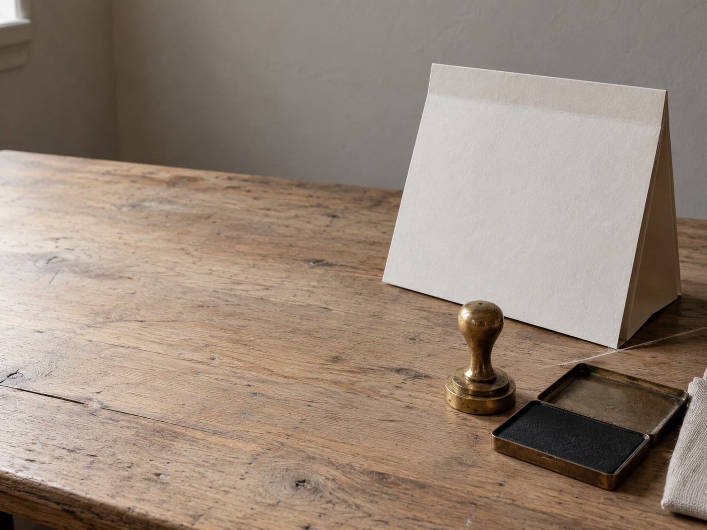 A folded paper calendar page beside a small brass stamp and an ink pad on a wooden desk.