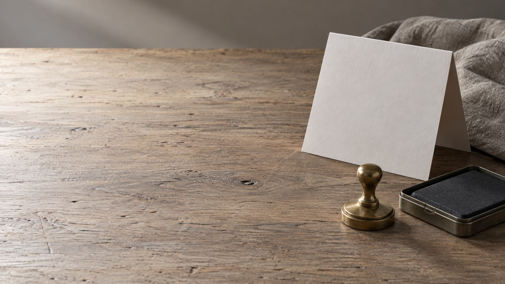 A folded paper calendar page beside a small brass stamp and an ink pad on a wooden desk, in soft light.