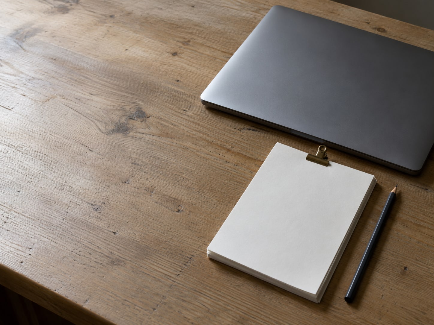 A closed laptop beside a neat stack of paper invoices held by a small metal clip, next to a pencil.