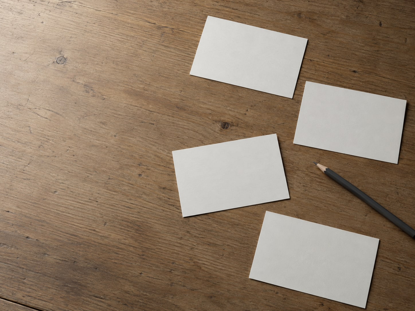 A small stack of blank index cards and a pencil laid out on a desk, each card set apart from the others.