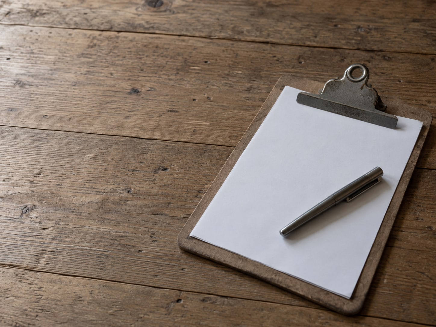A blank paper order form and a closed pen resting on a clipboard on a plain wooden counter.