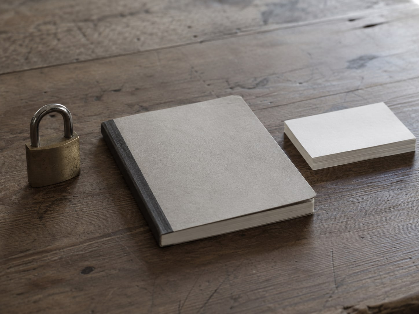 Un solo candado de latón junto a una libreta y una pequeña pila de fichas en blanco sobre una mesa de madera.