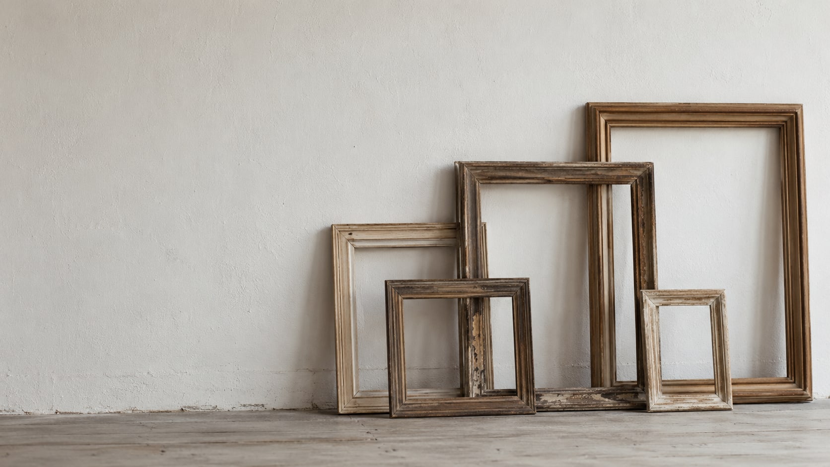 Una fila de marcos de fotos de madera vacíos, de distintos tamaños, recargados contra una pared lisa pintada.