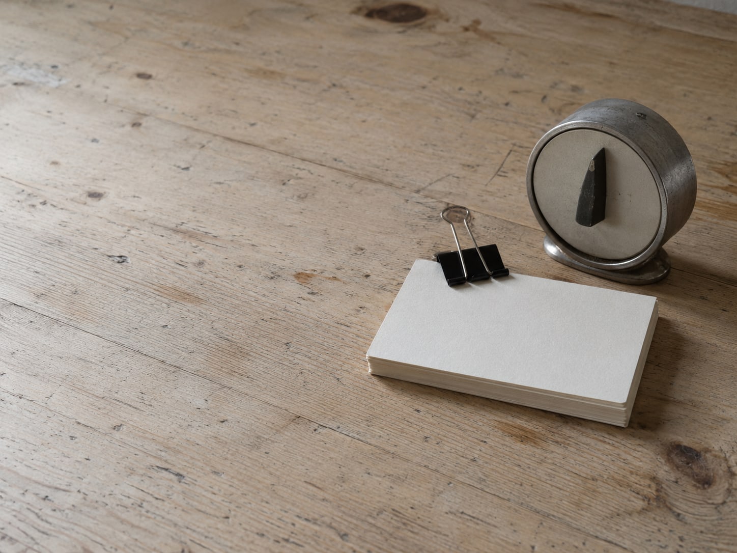 A stack of blank index cards held with a plain binder clip next to a small mechanical kitchen timer.