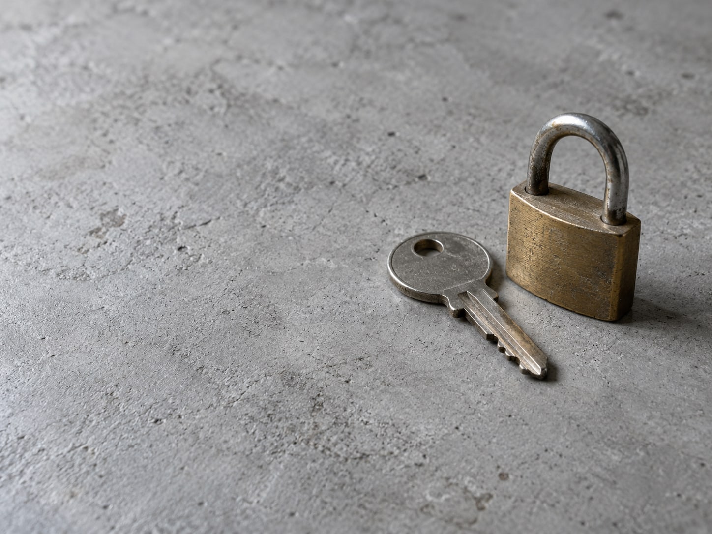 A single paper house key and a small brass padlock lying on a plain gray table surface.