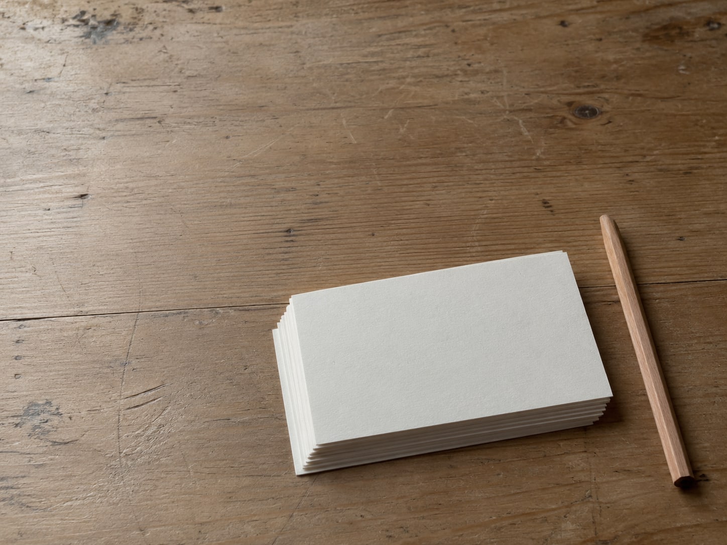 A tidy row of blank index cards on a wooden desk beside a plain wooden pencil.
