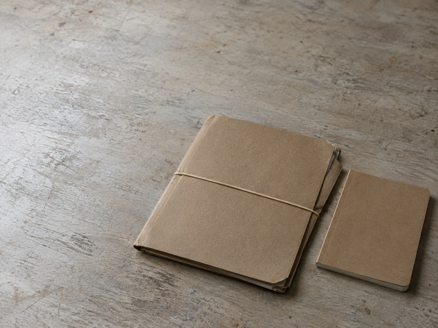 A cardboard document folder with a rubber band around it beside a closed notebook.