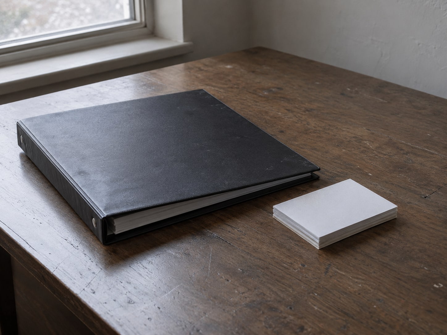 A closed three-ring binder and a small stack of blank index cards on a quiet office desk.