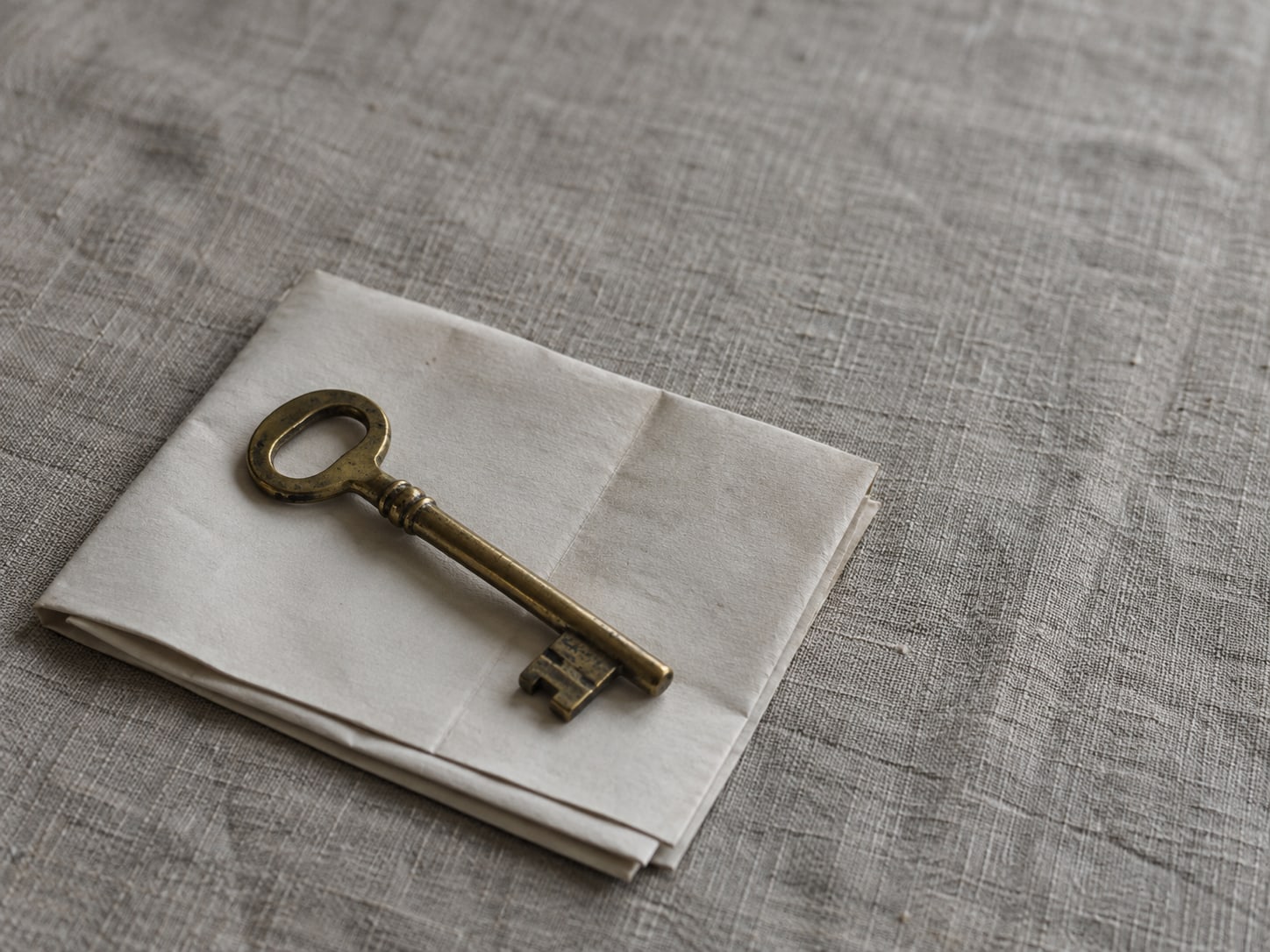 A single old brass key resting on a folded blank paper map on a gray linen tablecloth.