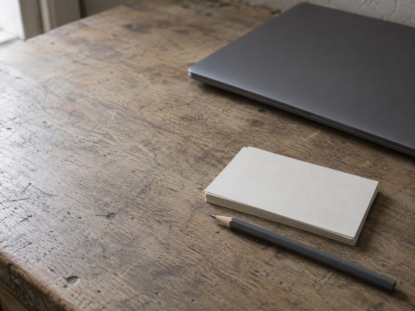 A small stack of blank index cards and a pencil beside a closed laptop on a desk.