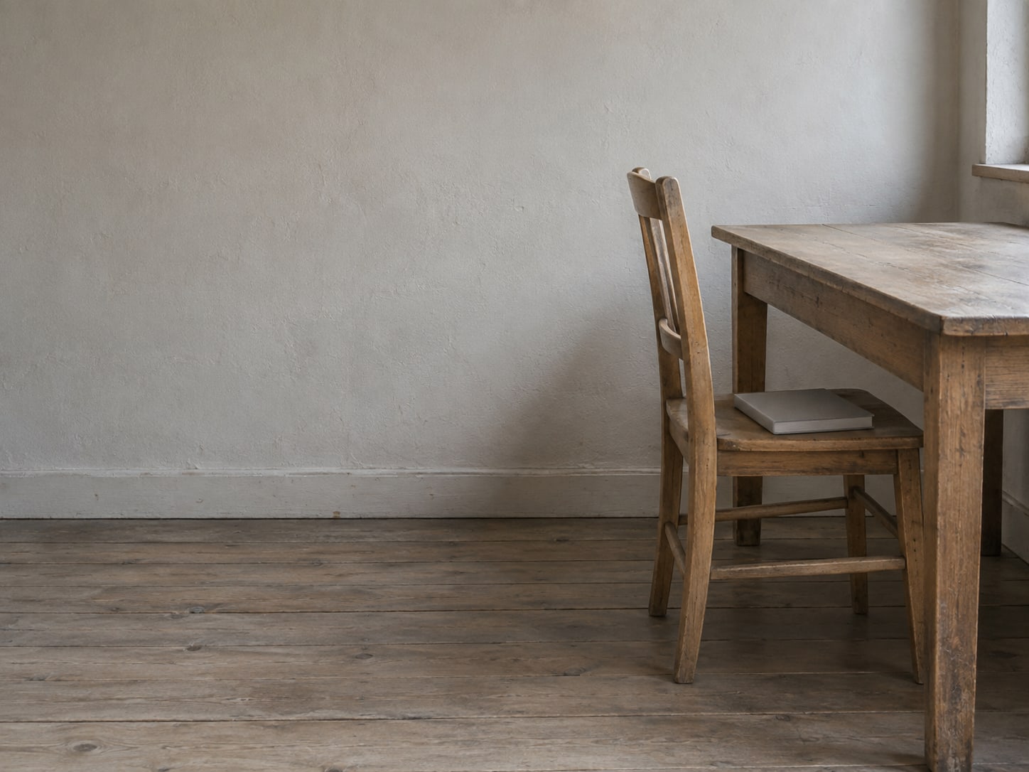 An empty wooden chair pushed in at a desk with a single closed notebook on the seat.
