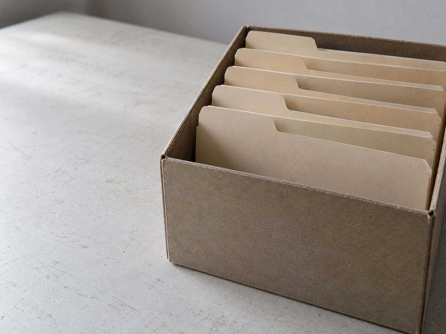 Five manila folders standing upright in an open file box, their tabs blank.