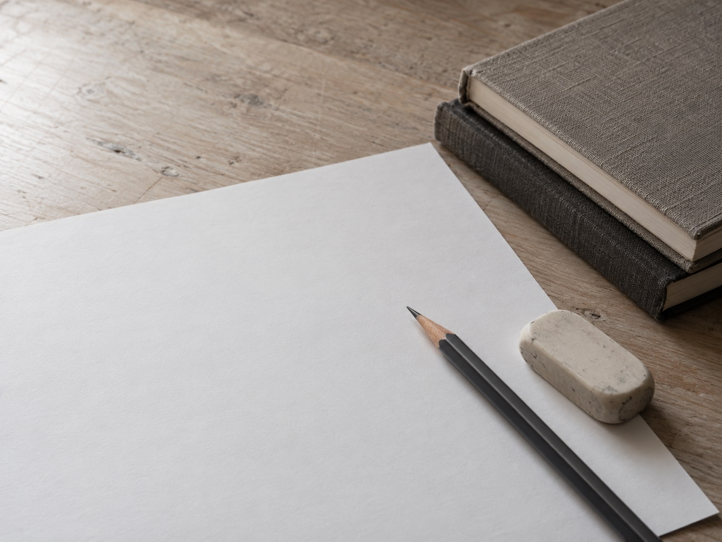A pencil and a soft eraser lying on a sheet of blank paper beside a small stack of closed notebooks.