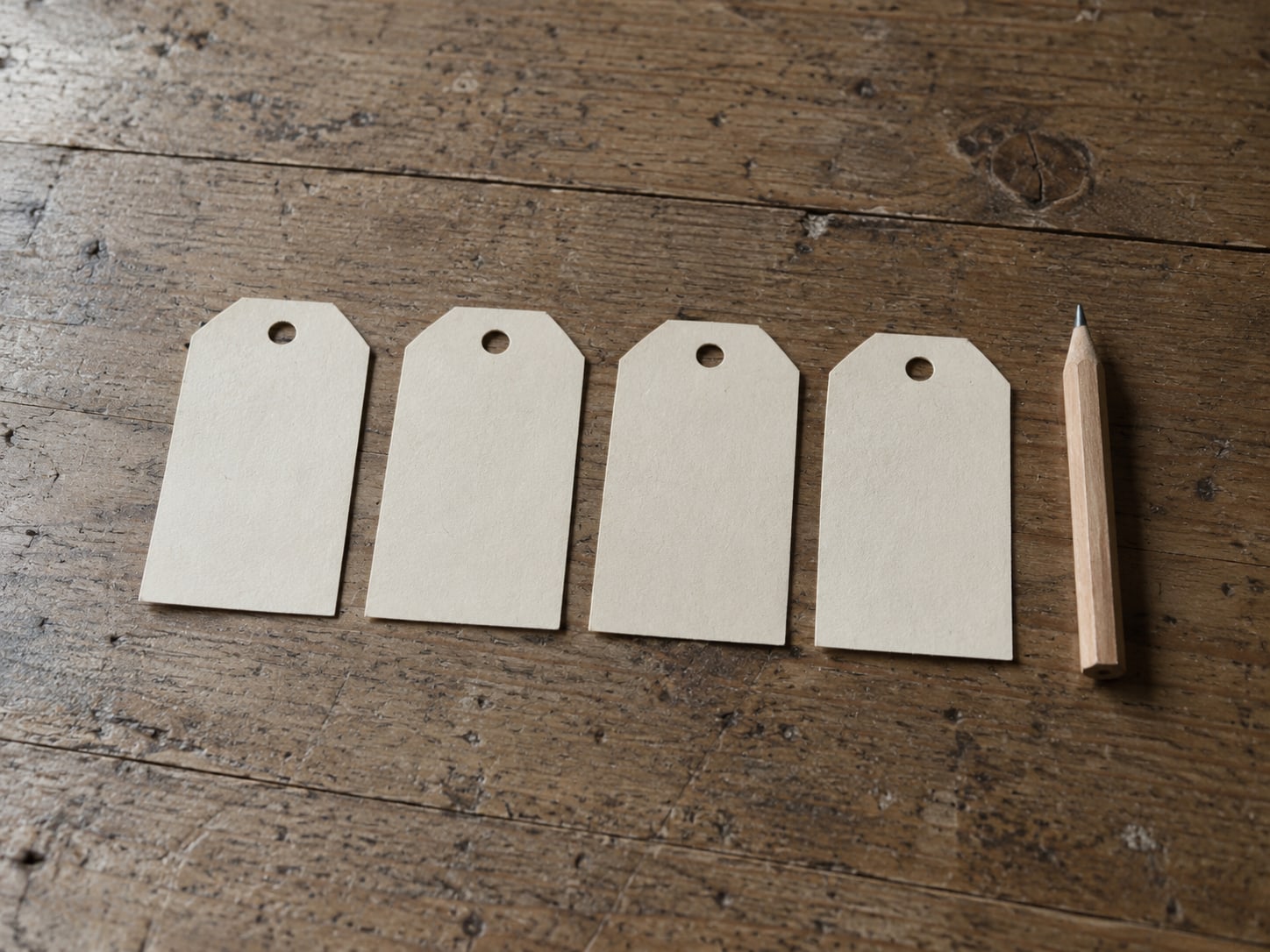 Una fila de etiquetas de papel en blanco para equipaje y un lápiz pequeño alineados sobre una mesa de madera gastada.