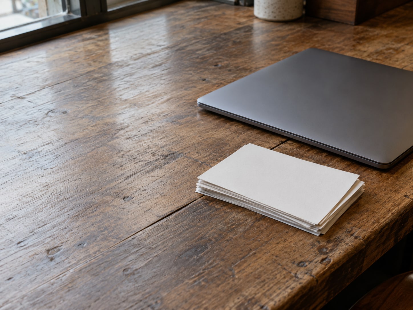 A closed laptop beside a small stack of blank printed menu cards on a wooden restaurant counter.