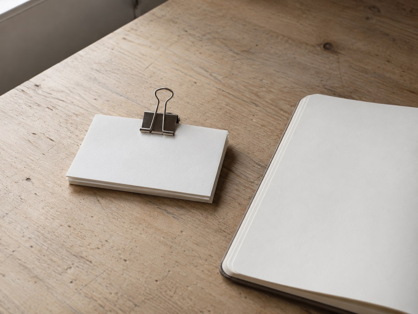 A small stack of index cards held with a binder clip beside a clean empty notebook page on a desk.