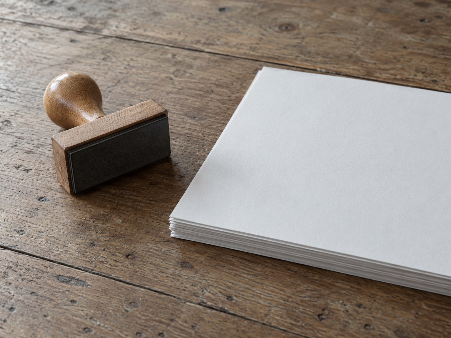 A blank rubber stamp resting beside an unmarked stack of paper on a worn wooden desk.