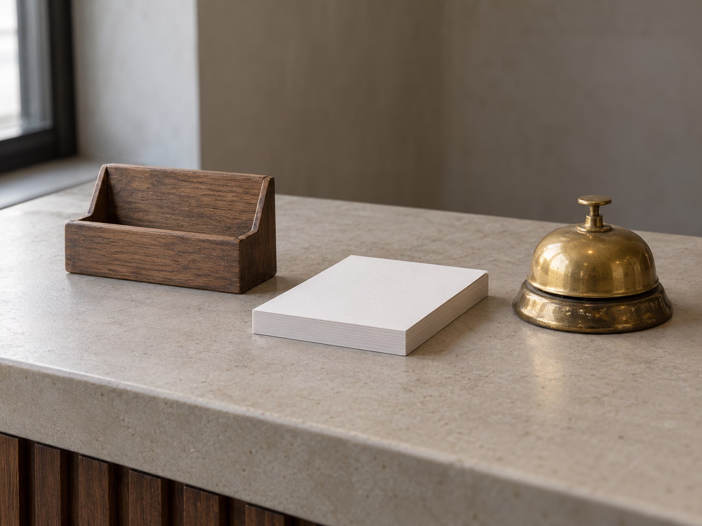 A wooden appointment card holder, an unused paper receipt pad and a small brass bell on a plain counter.