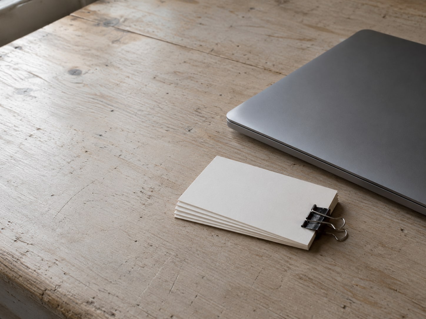 A small stack of index cards held by a binder clip next to a closed laptop on a plain table.