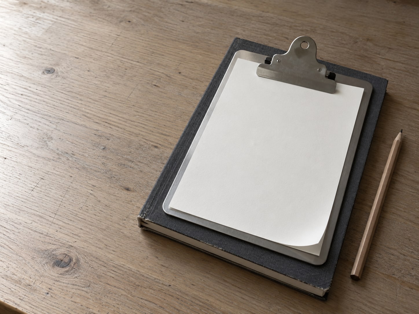 A clipboard with a blank checklist sheet resting on a closed notebook and a pencil.