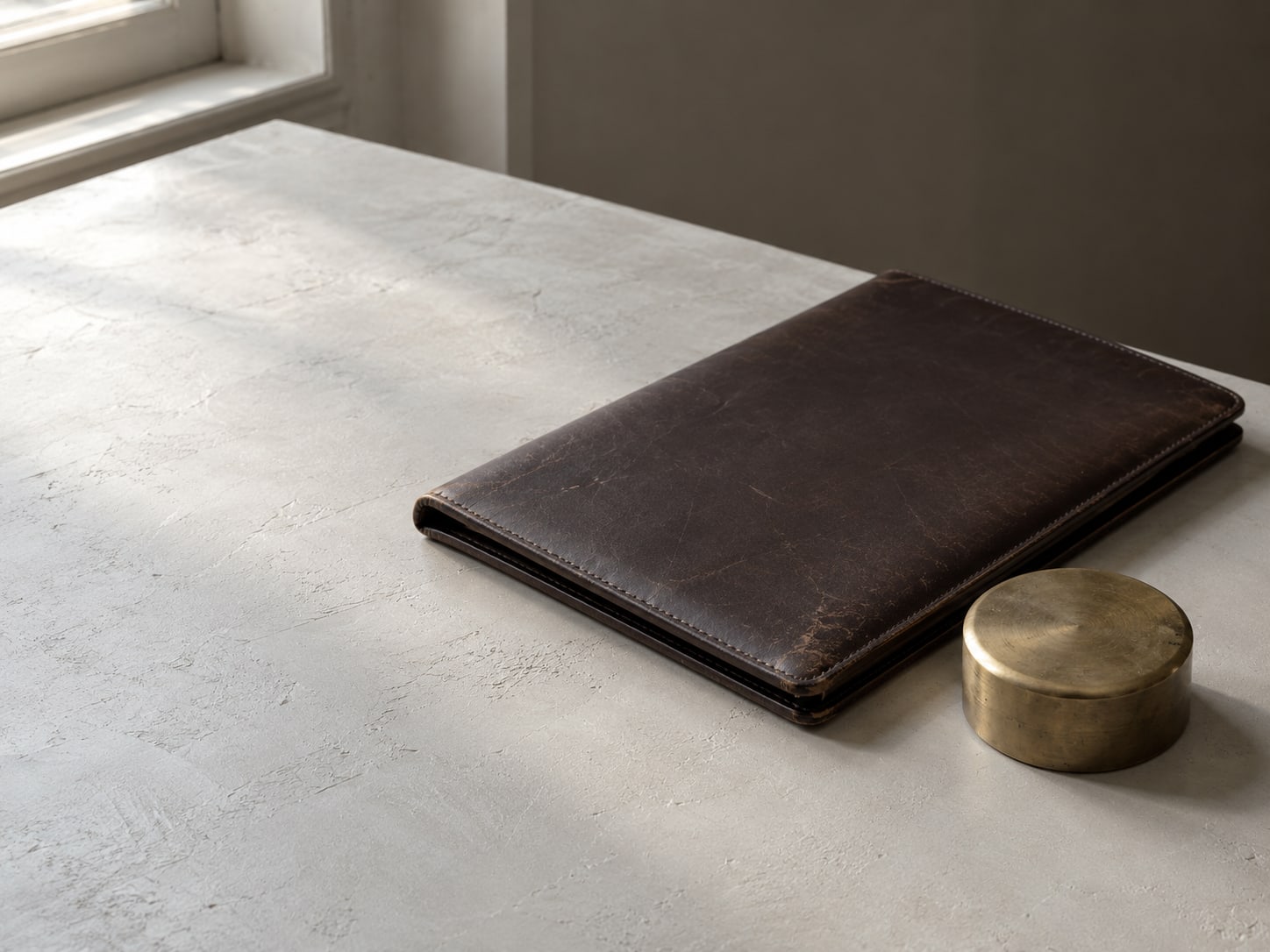 A closed leather folder beside a brass paperweight on a clear desk.