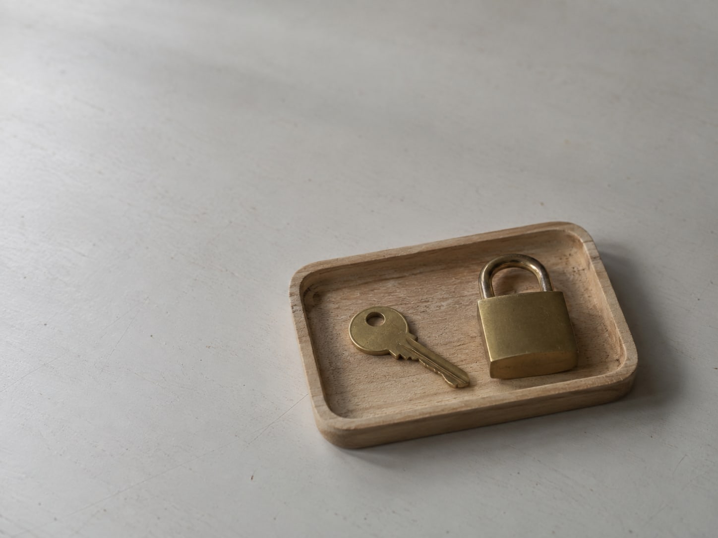 A single brass key on a small wooden tray beside a closed padlock on a plain desk.