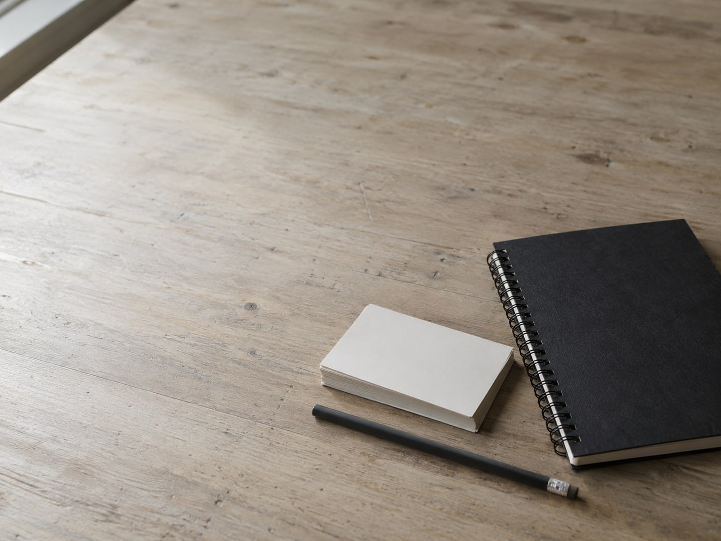 A small stack of blank index cards and a pencil beside a closed spiral notebook on a clean desk.