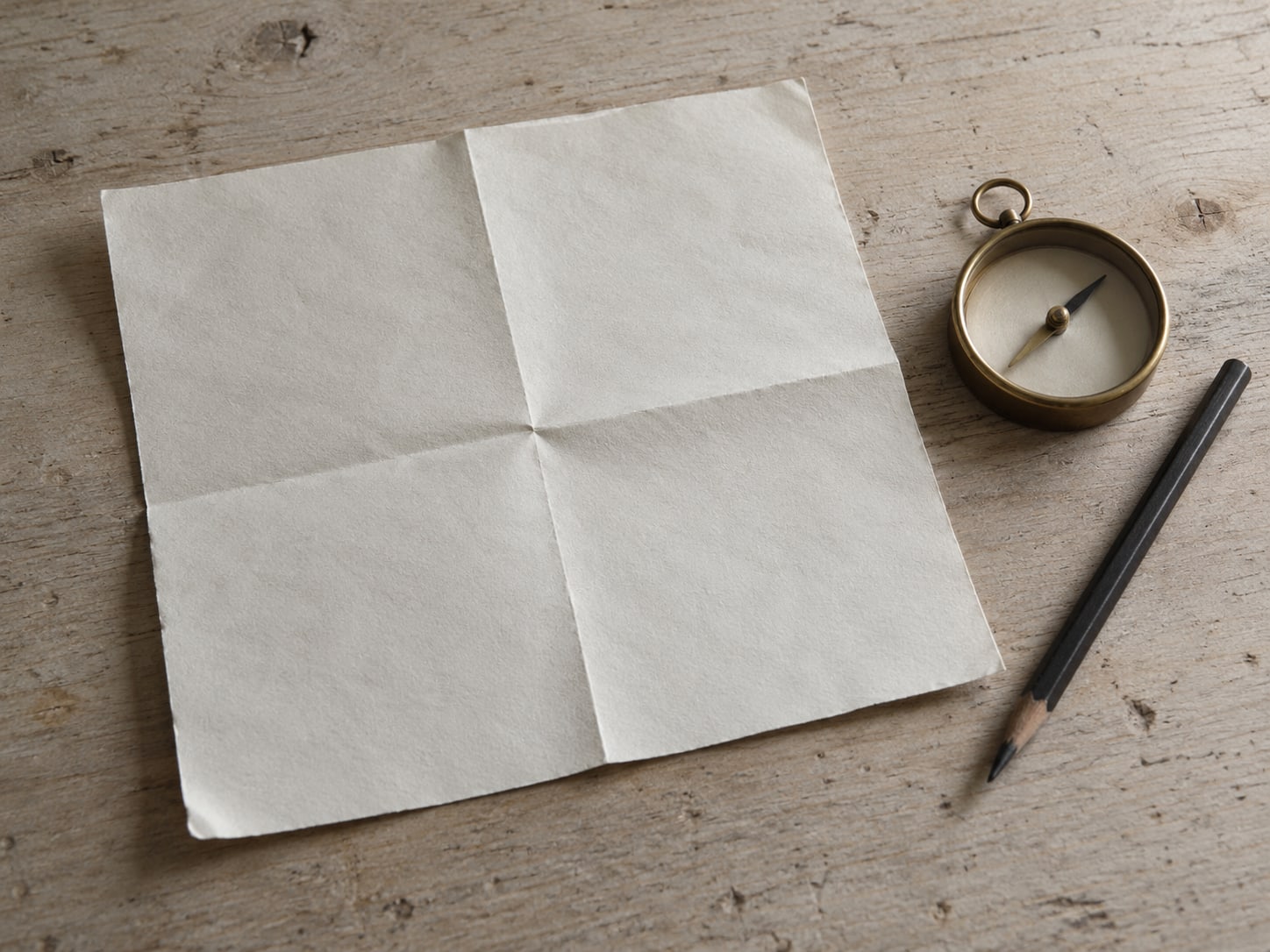 A paper map folded in quarters next to a small brass compass and a pencil on a pale table.