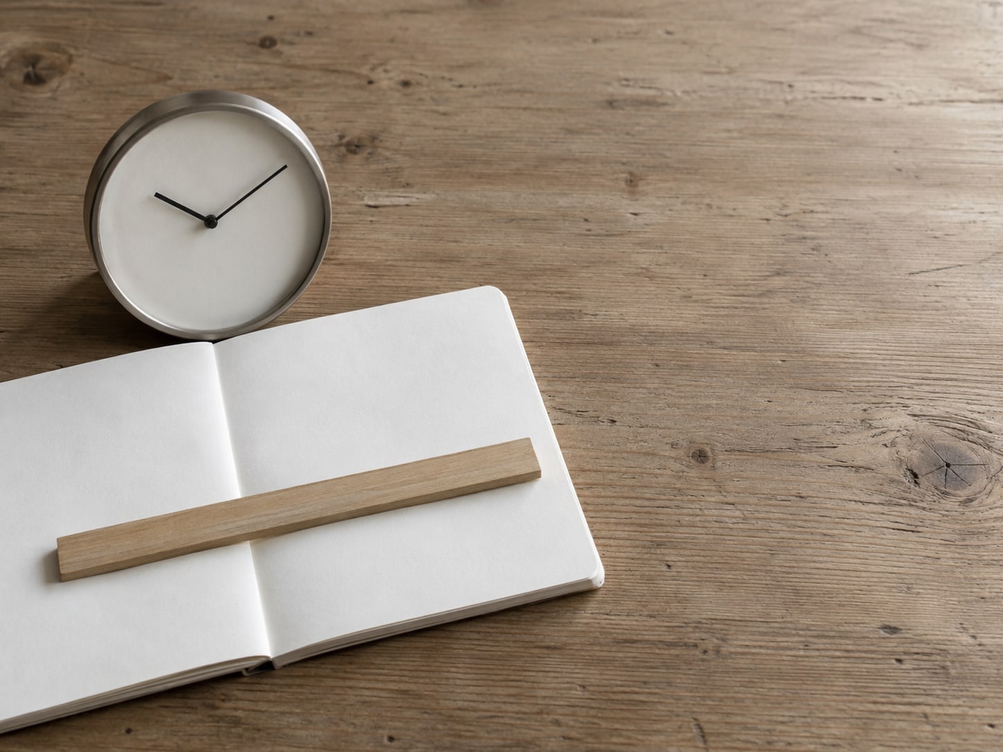 A single ruler laid across a blank notebook page next to a plain wall clock, no numbers visible.