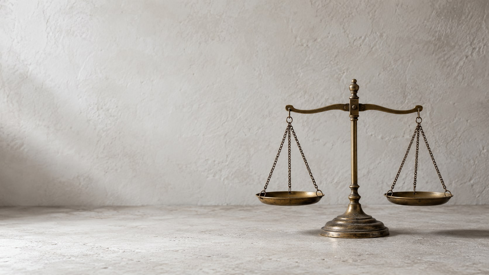 A pair of metal scales with two empty brass dishes sitting level on a plain pale surface.