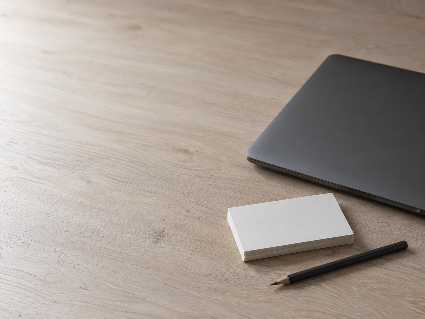 A closed laptop and a small stack of blank index cards beside a pencil on a clean desk.