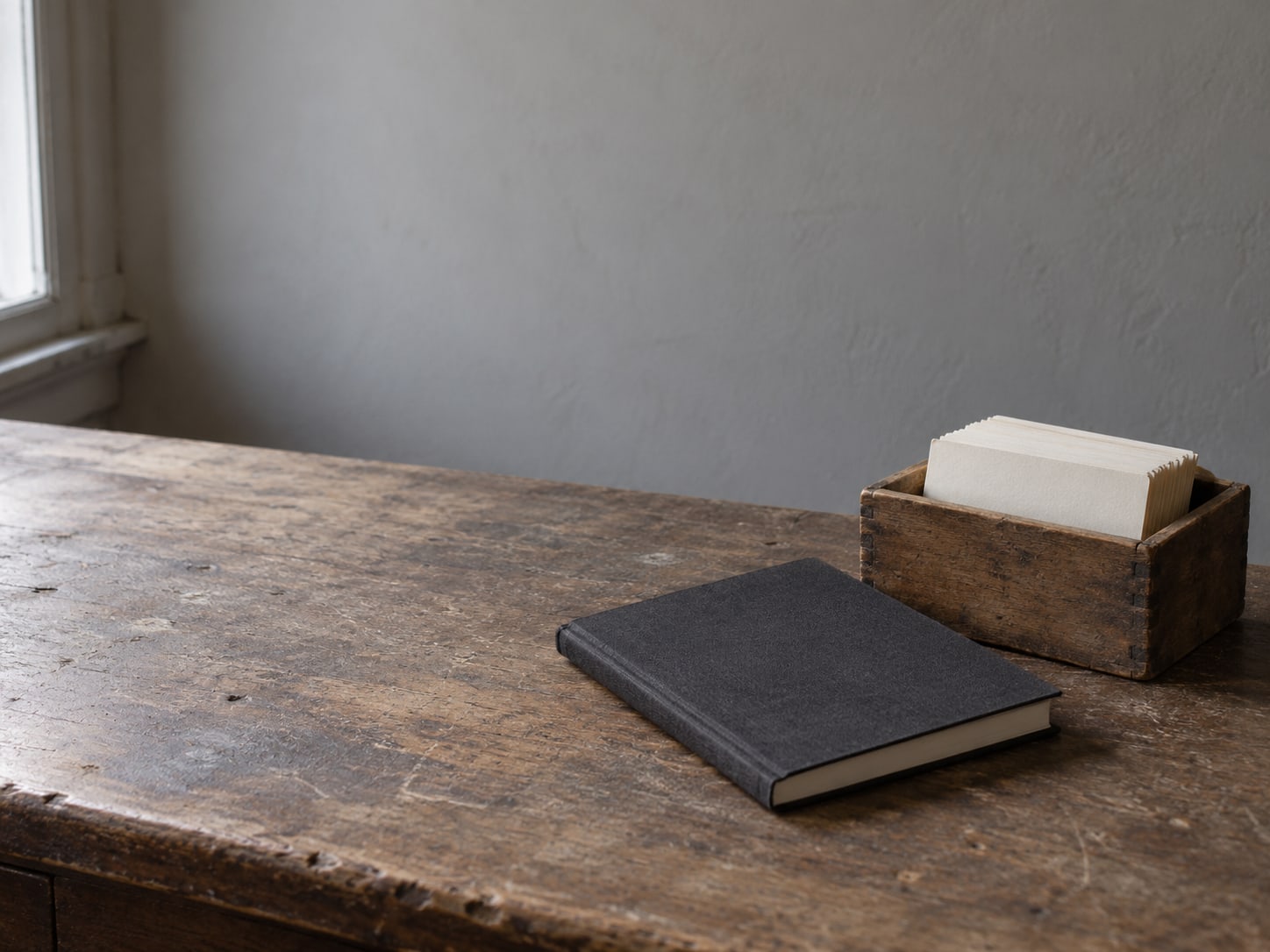 Un cuaderno cerrado junto a una pequeña caja de madera con fichas en blanco sobre un escritorio sencillo.