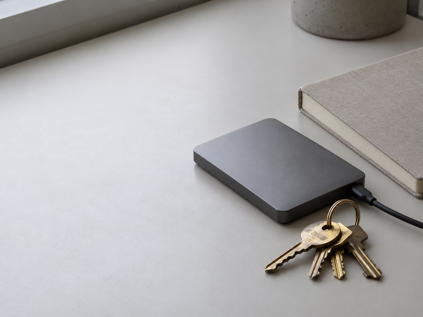 A small external drive and a ring of brass keys resting on a clean desk beside a closed notebook.