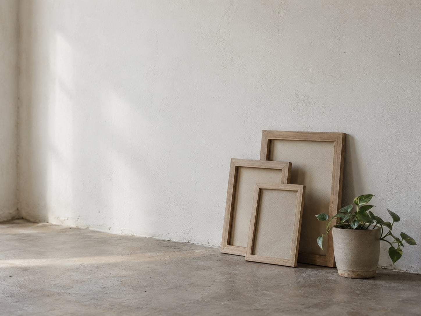 A stack of blank wooden frames leaning against a plain wall beside a small potted plant.