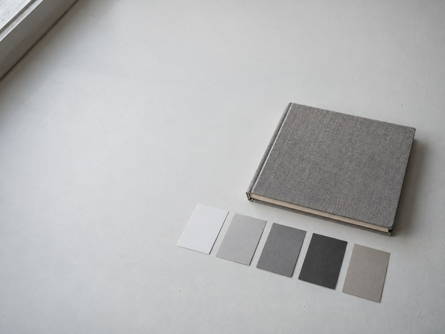 A closed sketchbook beside a row of small paint sample cards on a clean white table.