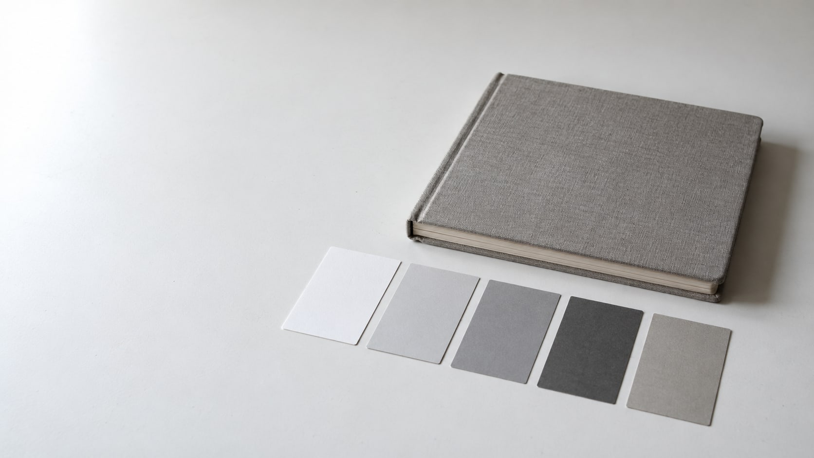 A closed sketchbook beside a row of small paint sample cards on a clean white table.