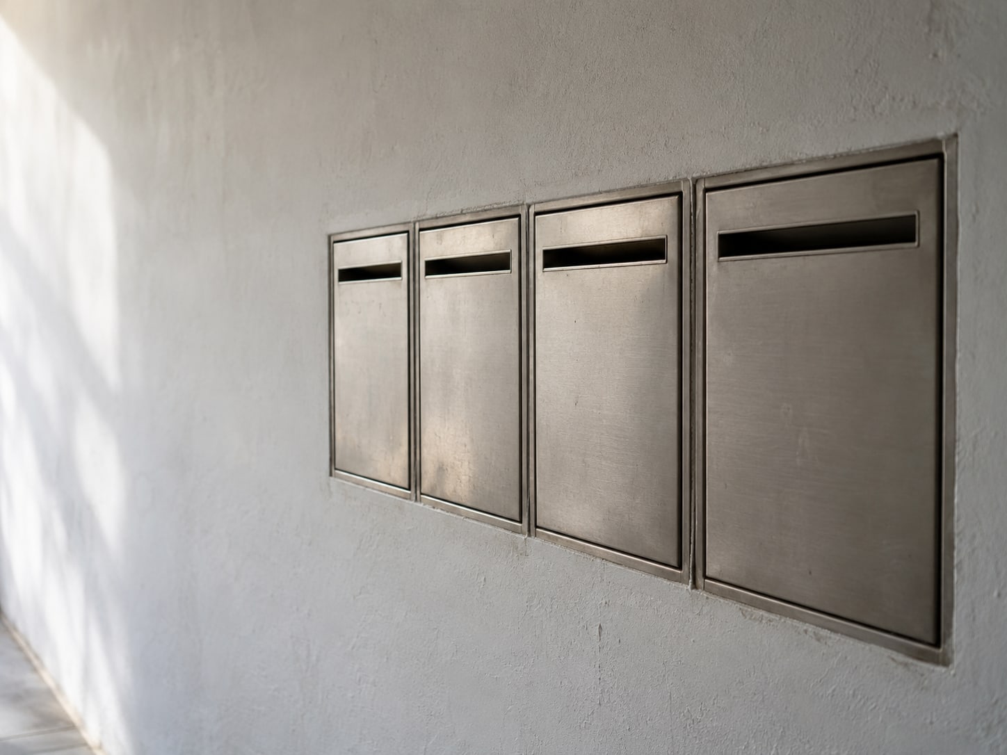 Una fila de pequeñas puertas metálicas cerradas de buzón sobre una pared lisa, cada una con una ranura vacía y sin etiquetas.