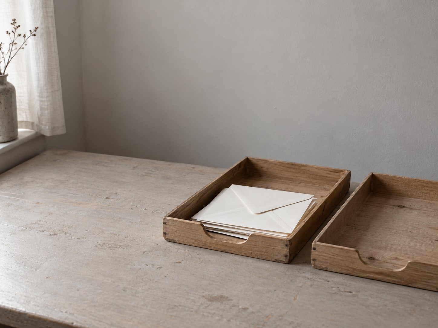 Two shallow wooden trays on a desk, one holding sealed envelopes and the other empty