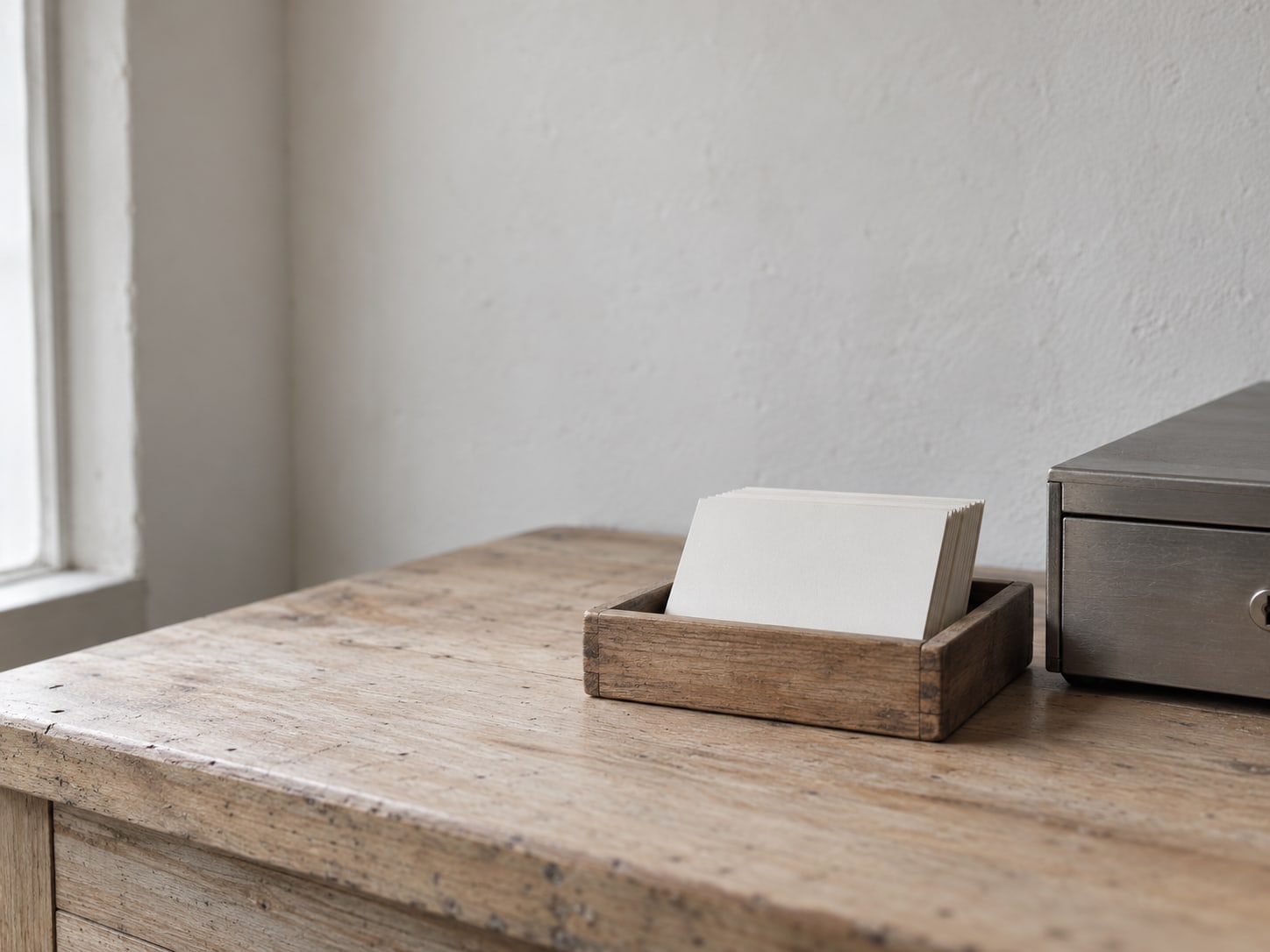 A small stack of blank cards in a wooden tray next to a tidy cash drawer on a shop counter.