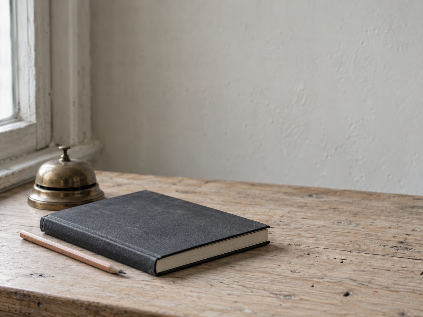 A closed appointment book beside a pencil and a small brass desk bell on a wooden counter.
