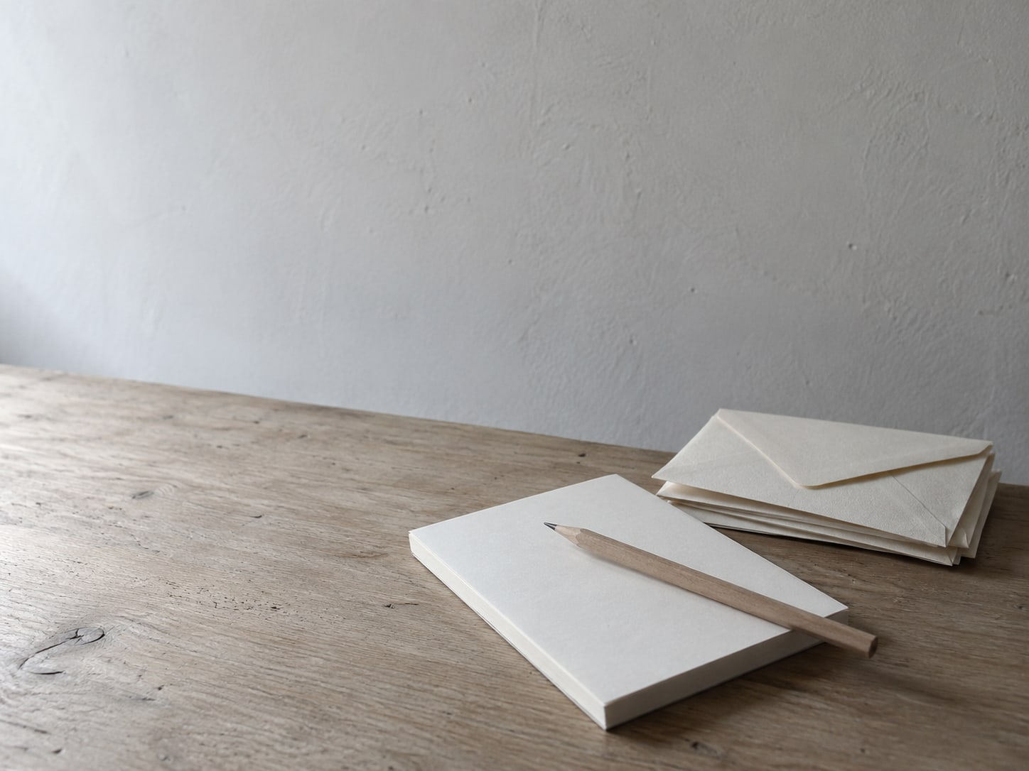 A pencil lying across a blank notepad beside a small stack of folded paper envelopes.